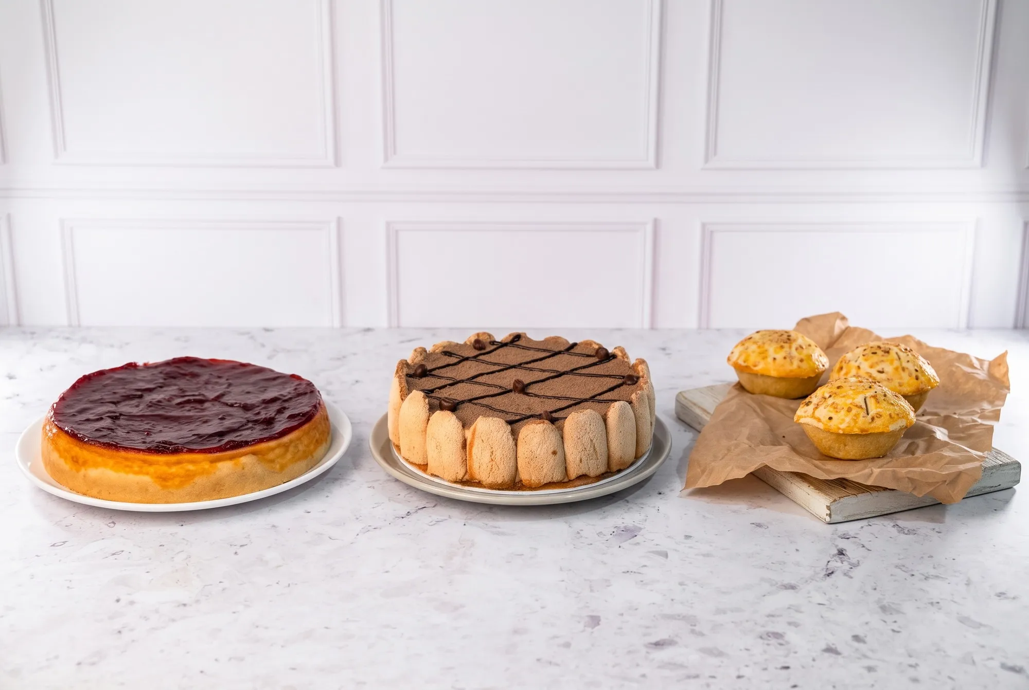 Cheesecake de frutas vermelhas, torta tiramisu e empadas de frango sobre bancada de mármore